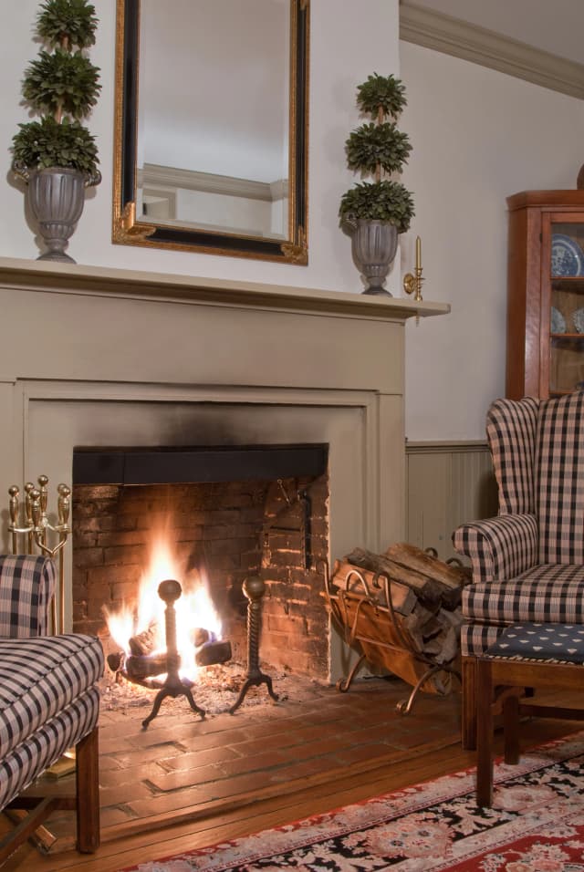 A living room with a lit fireplace framed by an elegant mantel. Two striped armchairs and a rug create a warm, inviting atmosphere.